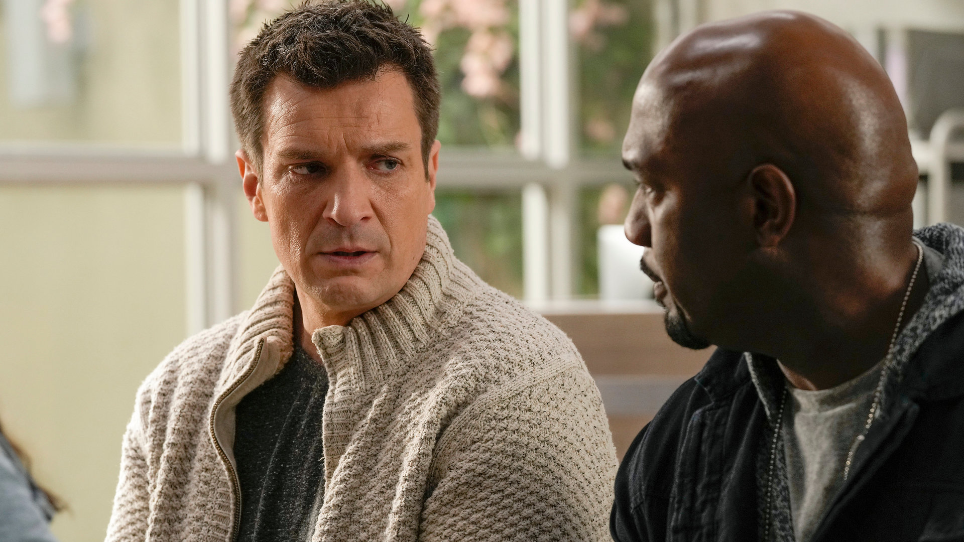 "The Rookie - Gebrochene Herzen": Nolan (Nathan Fillion) sitzt neben Sergeant Grey (Richard T. Jones) in einem Wartezimmer und schaut ihn niedergeschlagen an.