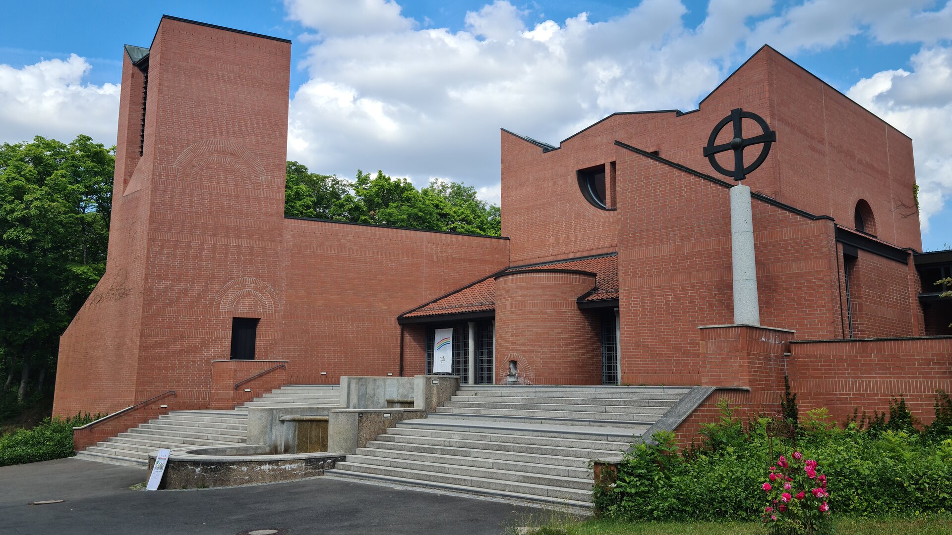 "Evangelischer Gottesdienst - Himmelhoch und tief verwurzelt": Außenansicht des Klosters Schwanberg in Unterfranken: Bei dem modernen, architektonisch interessant gestalteten Gebäude aus roten Backstein führt eine breite graue Treppe zum Eingang, der Turm ist etwas nach vorne versetzt.