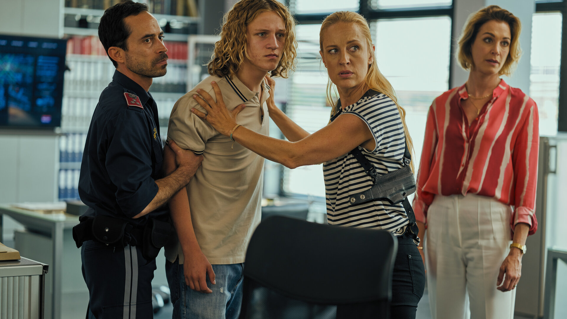 "SOKO Wien - Klare Fakten": Jo Schneider (Lorenz Pojer) steht im Polizeipräsidium zwischen Penny Lanz (Lilian Klebow) und einem Polizisten (Komparse). Penny hält Jo an den Schultern fest und der Polizist hat seinen rechten Arm fest im Griff. Links seitlich hinter Penny steht die Klara Schneider (Julia Stinshoff).