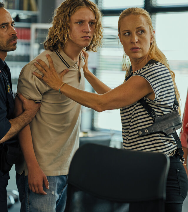 "SOKO Wien - Klare Fakten": Jo Schneider (Lorenz Pojer) steht im Polizeipräsidium zwischen Penny Lanz (Lilian Klebow) und einem Polizisten (Komparse). Penny hält Jo an den Schultern fest und der Polizist hat seinen rechten Arm fest im Griff. Links seitlich hinter Penny steht die Klara Schneider (Julia Stinshoff).