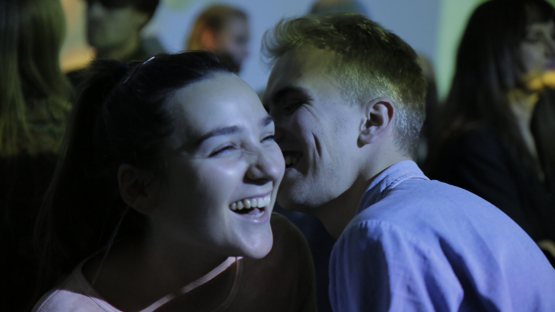 "About Saturday - Der Barkeeper": Klara (Darin Hagi) HM (William Greni Arnø) tanzen in einem Club eng zusammen auf einer Tanzfläche inmitten vieler Menschen. Klara lacht, während HM ihr etwas ins Ohr flüstert.